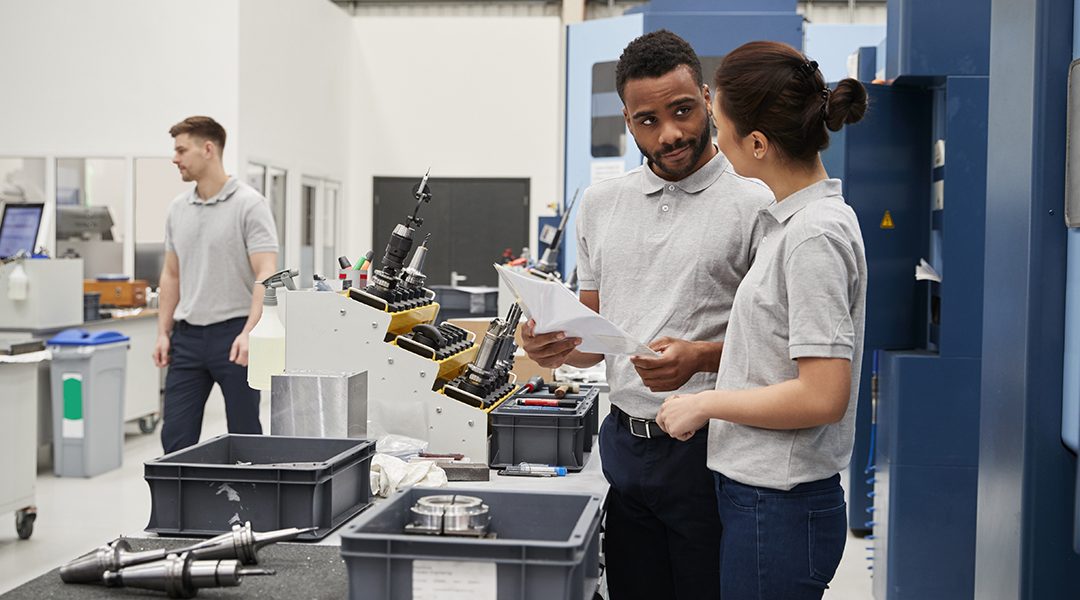 Engineer And Apprentice Meet On Floor Of Precision Machining Shop