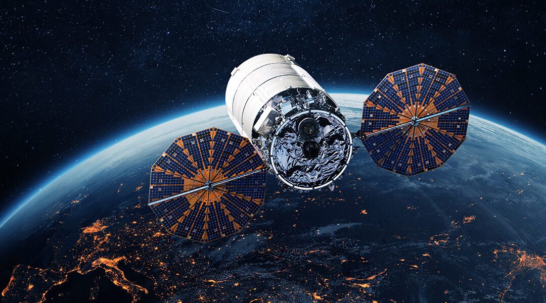 Satellite with two large solar arrays hovering above Earth's limb at night, city lights visible below.