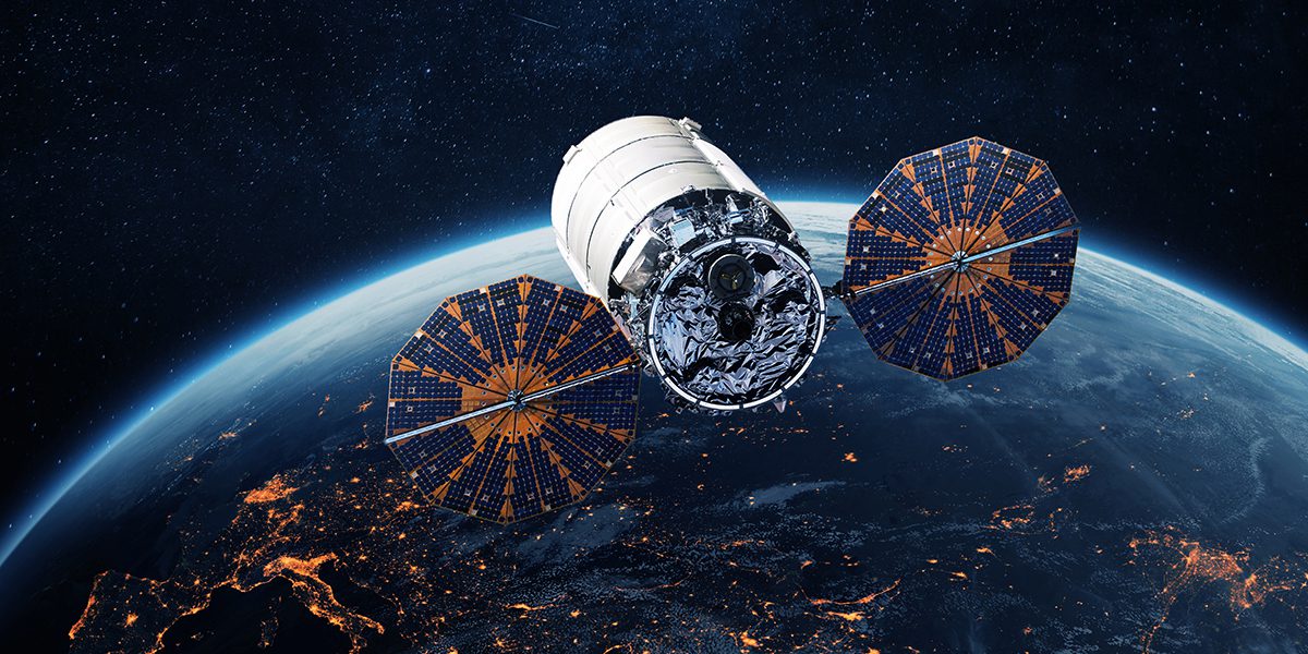 Satellite with two large solar arrays hovering above Earth's limb at night, city lights visible below.